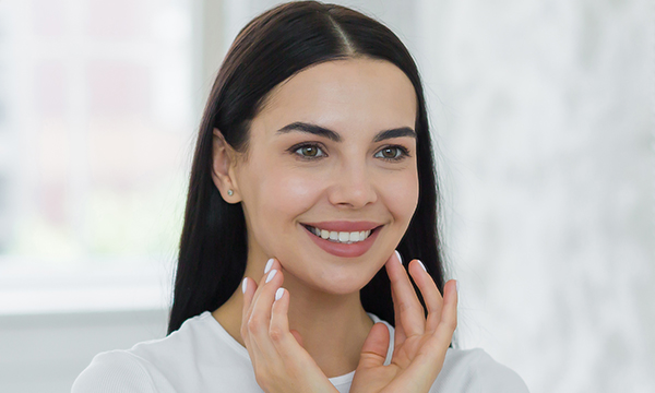 Woman smiling while touching her face in bright dental office setting.