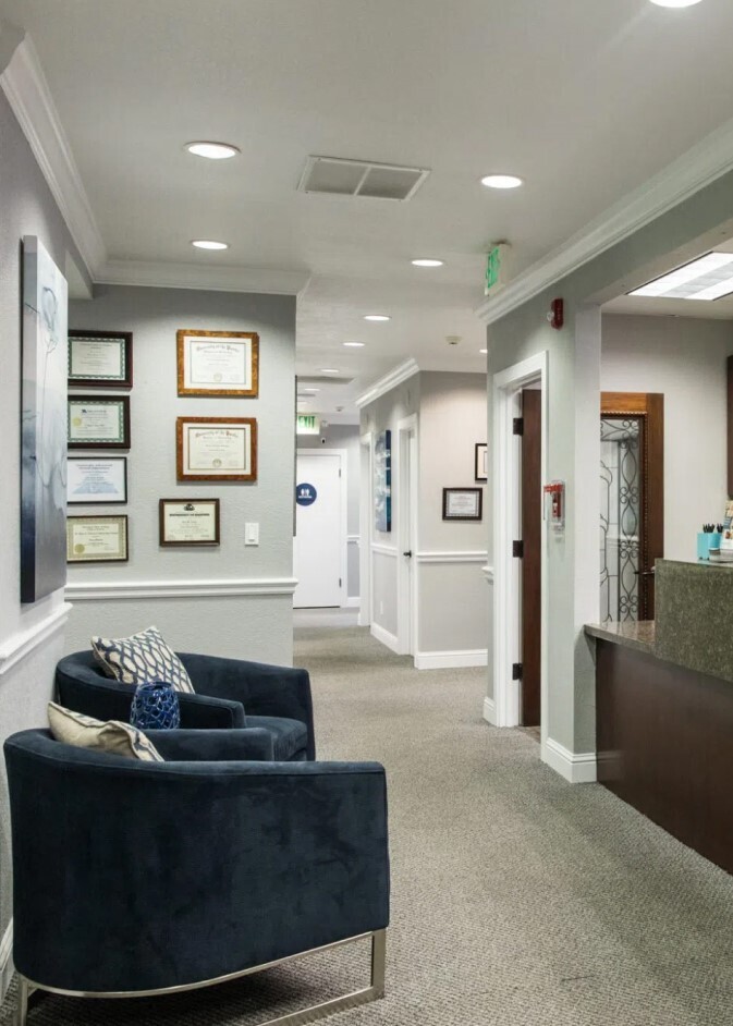 Modern dental office waiting room with comfortable seating and framed certifications on wall.