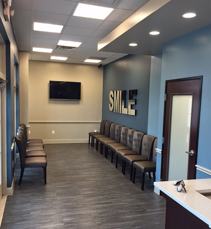 Modern dental waiting room with blue walls, seating, and illuminated SMILE sign