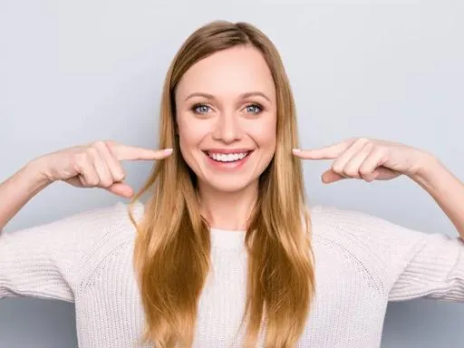 Woman smiling brightly while pointing to her teeth against white background.