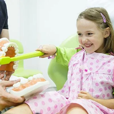 Young girl in pink pajamas smiling while playing with toy dental model at dentist office.