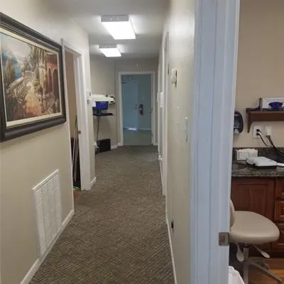 Hallway in dental office with white doors, carpet flooring, and framed artwork on walls.
