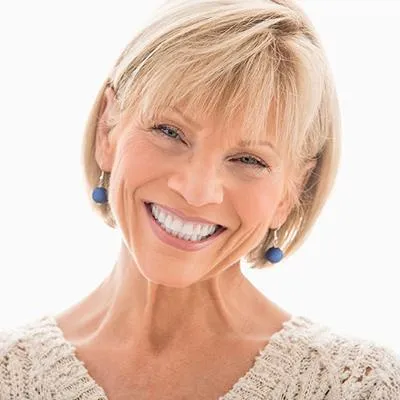 Smiling blonde woman in beige sweater against white background, professional headshot.