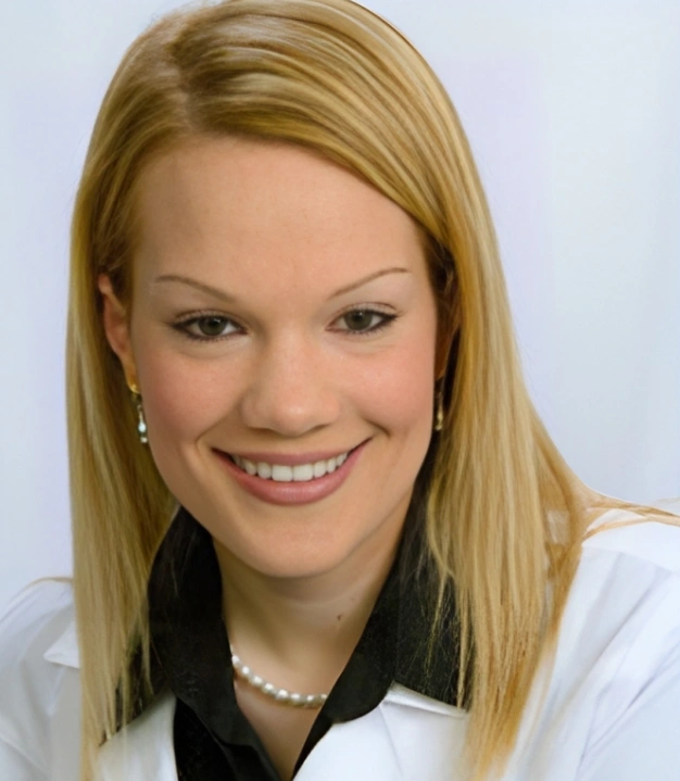 Professional headshot of smiling woman with blonde hair wearing white blazer and pearl necklace.