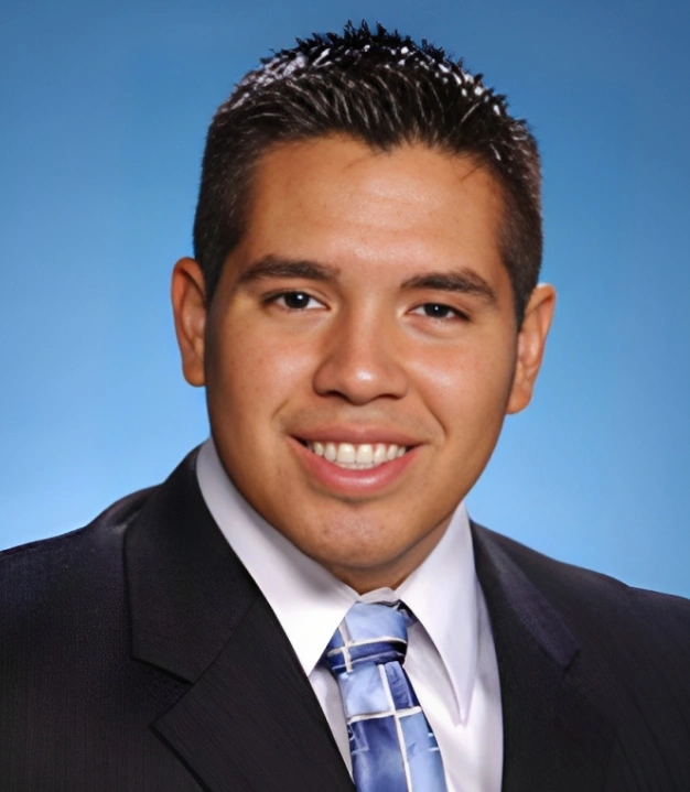 Professional headshot of male dental professional in business suit against blue background.
