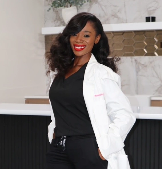 Professional woman in white coat and black top smiling in modern dental office setting.